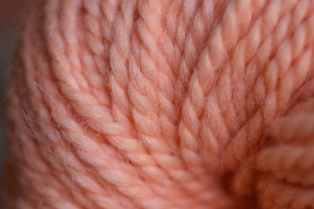 Close up of orange yarn twisting so it's reminiscent of a whirlpool. 