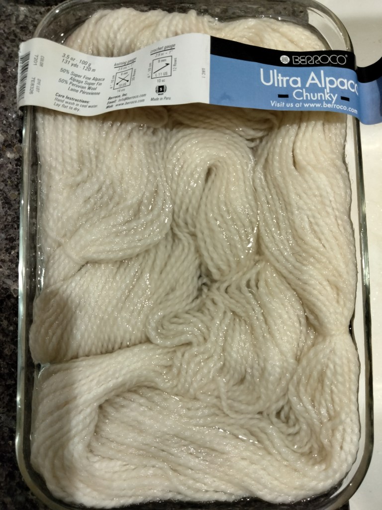 Rectangular glass pan with white yarn in water and Ultra Alpaca Chunky label across the top.