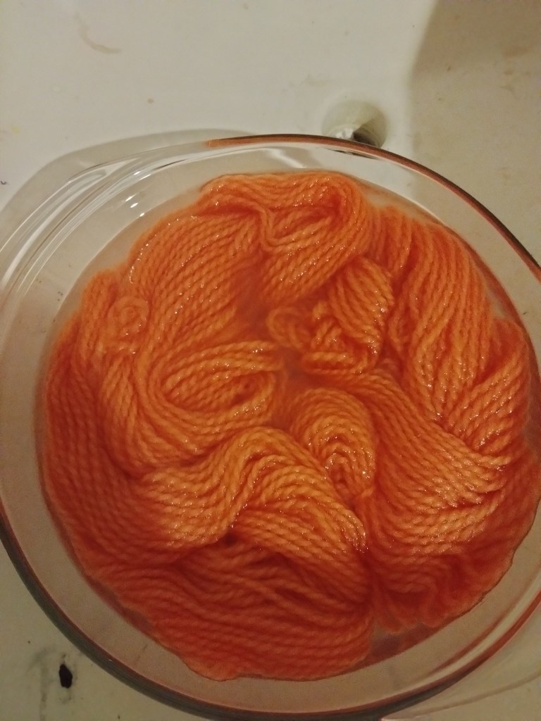 Glass casserole dish seen from above with water and orange yarn.
